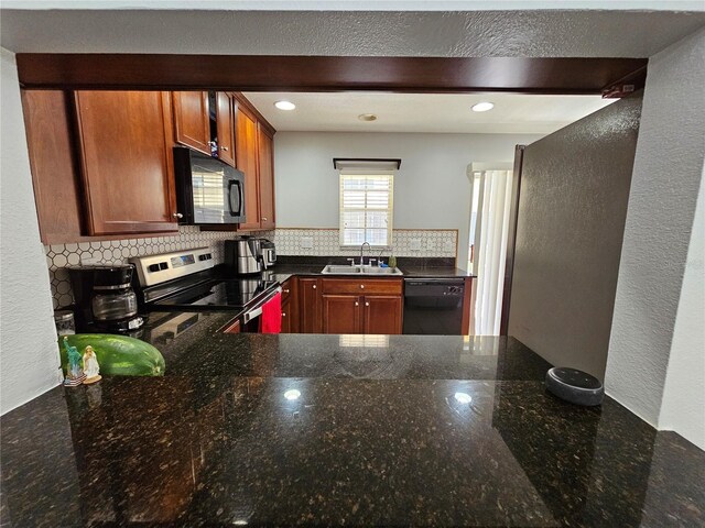 kitchen featuring dark stone countertops, stainless steel appliances, kitchen peninsula, backsplash, and sink