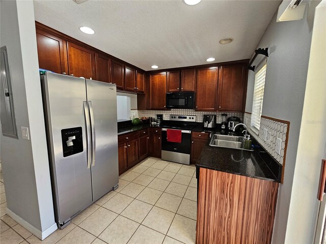 kitchen with dark stone countertops, stainless steel appliances, sink, tasteful backsplash, and light tile flooring