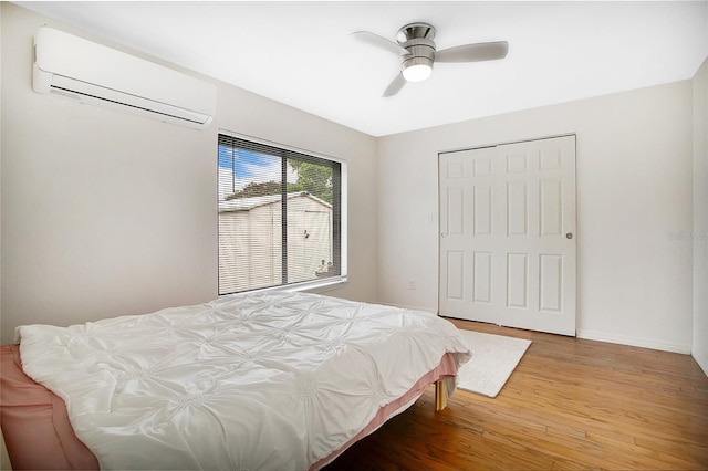 bedroom with a closet, hardwood / wood-style flooring, an AC wall unit, and ceiling fan