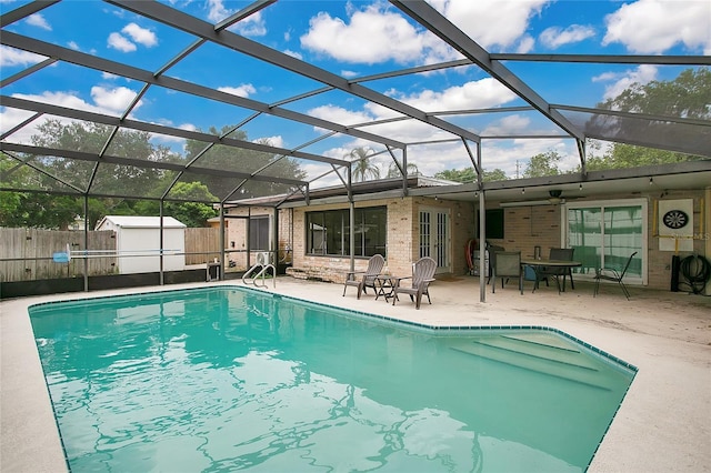 view of swimming pool with glass enclosure, a storage unit, and a patio area