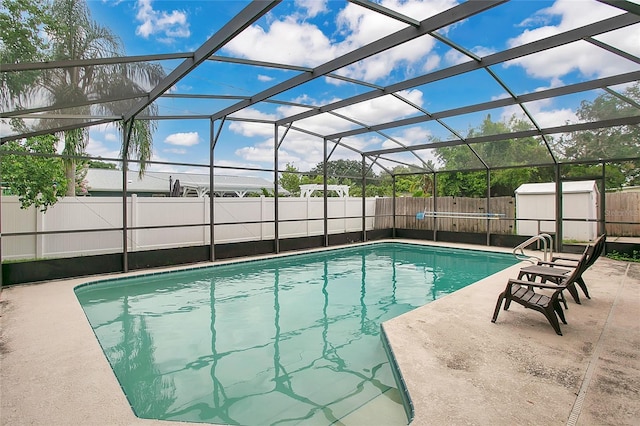 view of pool with glass enclosure, a storage shed, and a patio