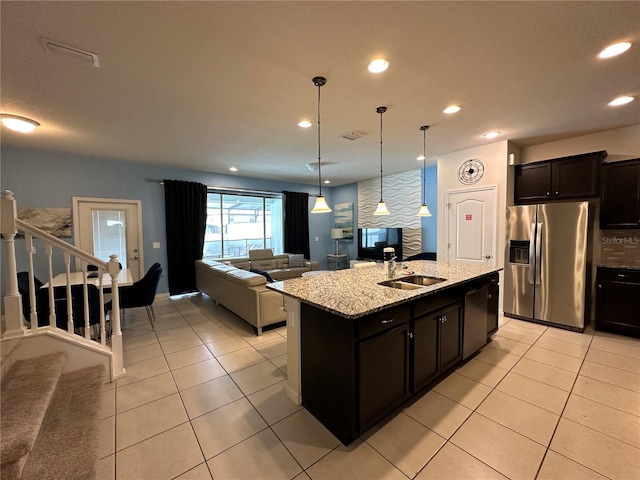 kitchen with stainless steel refrigerator with ice dispenser, light stone counters, sink, pendant lighting, and a center island with sink