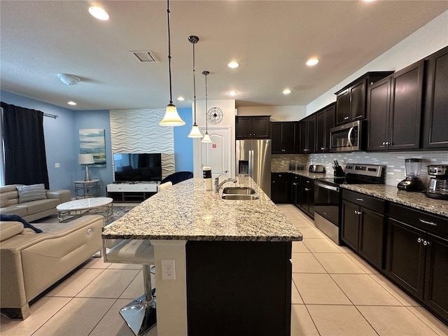 kitchen featuring stainless steel appliances, light stone counters, an island with sink, decorative light fixtures, and a breakfast bar