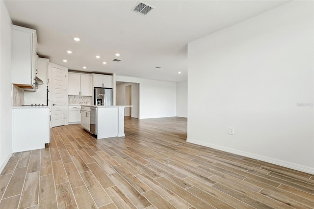 kitchen featuring appliances with stainless steel finishes, backsplash, light hardwood / wood-style floors, white cabinetry, and an island with sink