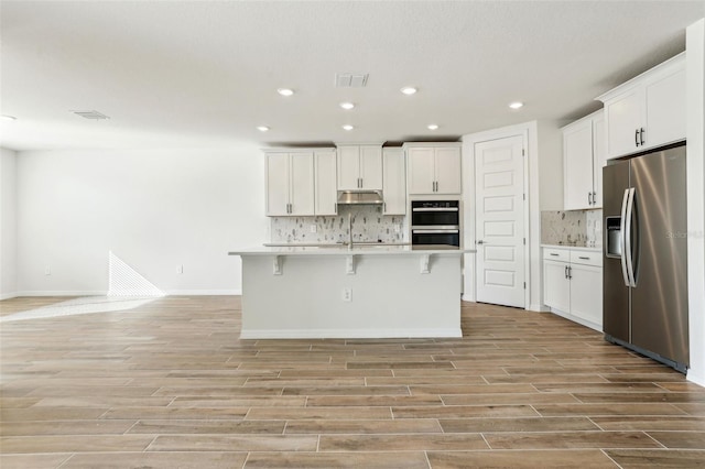 kitchen featuring a center island with sink, white cabinetry, backsplash, and appliances with stainless steel finishes