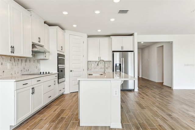 kitchen with white cabinetry, sink, stainless steel appliances, backsplash, and a center island with sink