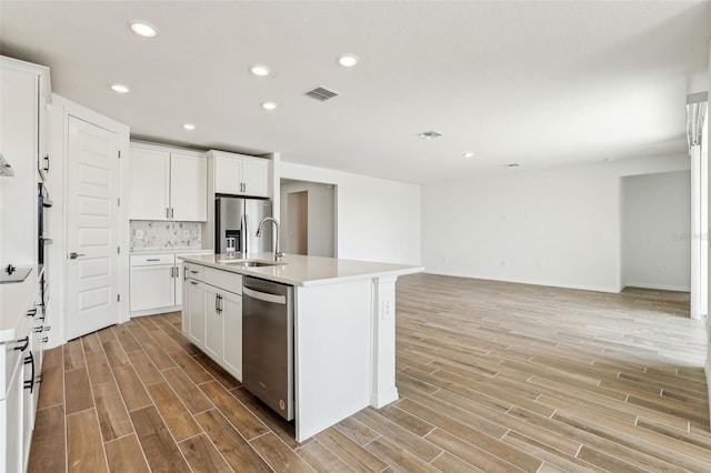 kitchen featuring a kitchen island with sink, white cabinets, sink, appliances with stainless steel finishes, and tasteful backsplash