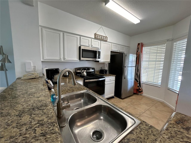 kitchen with appliances with stainless steel finishes, a textured ceiling, sink, light tile patterned floors, and white cabinetry