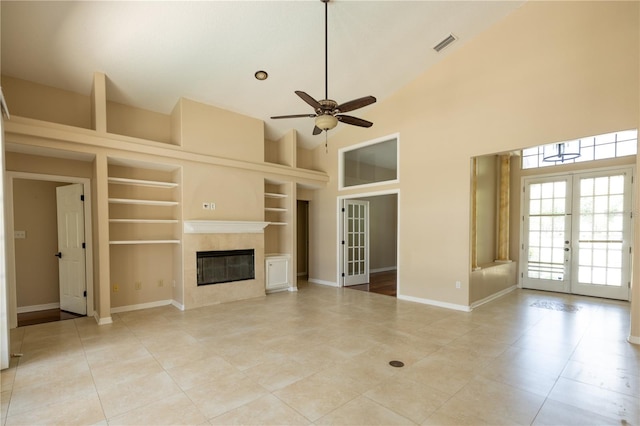 unfurnished living room featuring ceiling fan, high vaulted ceiling, a high end fireplace, built in shelves, and french doors