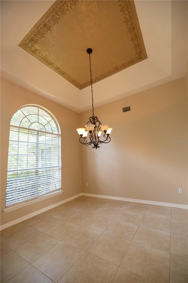 tiled spare room with a tray ceiling and a notable chandelier