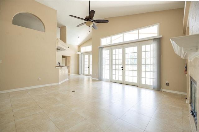 unfurnished living room featuring french doors, high vaulted ceiling, light tile patterned floors, a tile fireplace, and ceiling fan