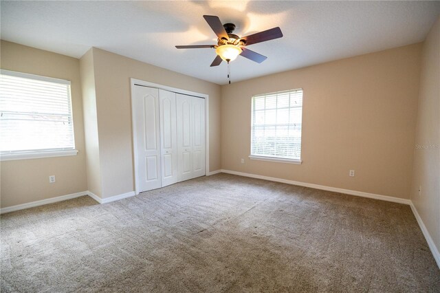 unfurnished bedroom with ceiling fan, a closet, carpet, and multiple windows