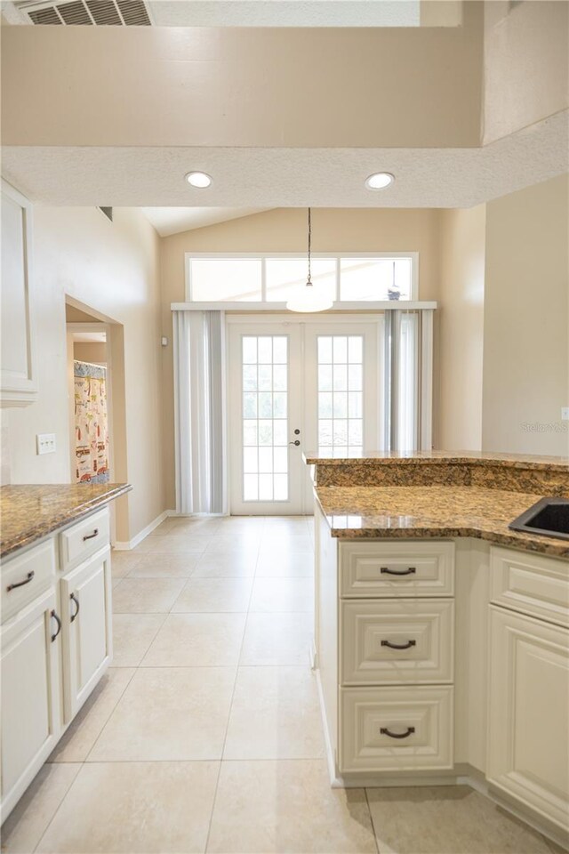 kitchen with vaulted ceiling, stone countertops, light tile patterned floors, and french doors