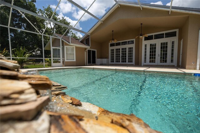 view of pool with glass enclosure, a patio area, ceiling fan, and french doors