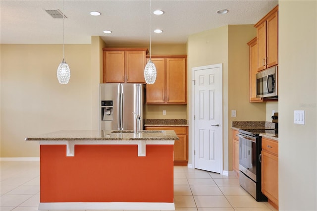 kitchen with light tile patterned flooring, an island with sink, sink, hanging light fixtures, and stainless steel appliances