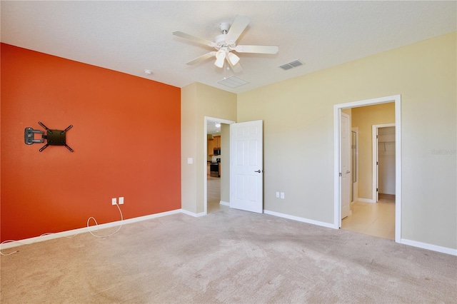 unfurnished bedroom with a spacious closet, light colored carpet, ceiling fan, and a textured ceiling