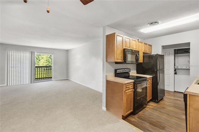 kitchen with stacked washer / dryer, dark colored carpet, and black appliances