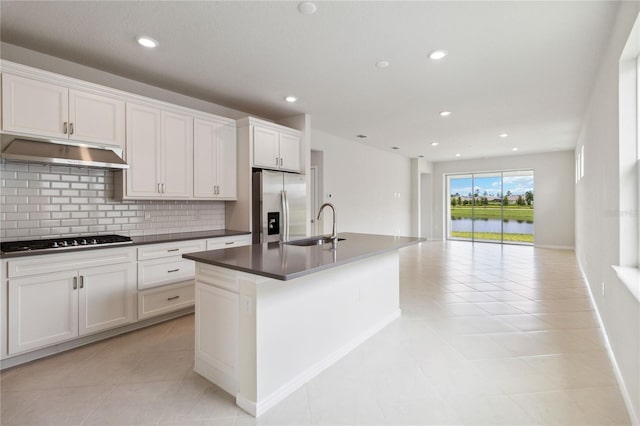 kitchen with backsplash, white cabinets, sink, stainless steel fridge, and an island with sink