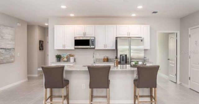 kitchen with light tile flooring, a kitchen island with sink, white cabinets, a breakfast bar, and appliances with stainless steel finishes