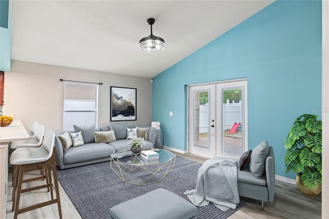 living room featuring light wood-type flooring, french doors, lofted ceiling, and a notable chandelier