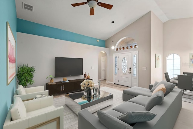 living room featuring arched walkways, visible vents, light wood-style flooring, a ceiling fan, and high vaulted ceiling