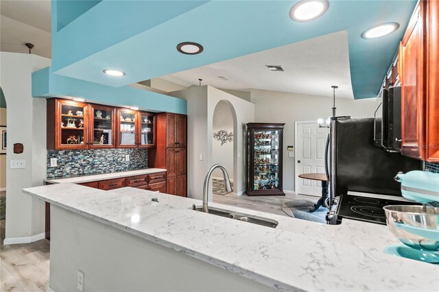 kitchen with light hardwood / wood-style floors, kitchen peninsula, sink, lofted ceiling, and light stone counters