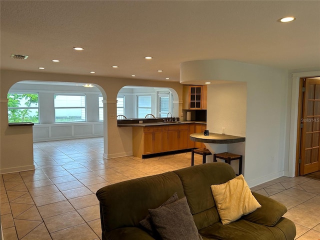 kitchen featuring light tile patterned flooring, a peninsula, a sink, open floor plan, and glass insert cabinets