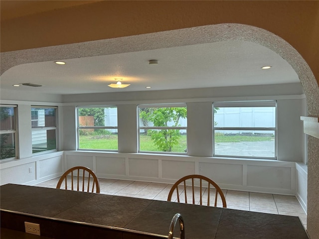 unfurnished dining area with visible vents, light tile patterned flooring, a textured ceiling, a decorative wall, and recessed lighting