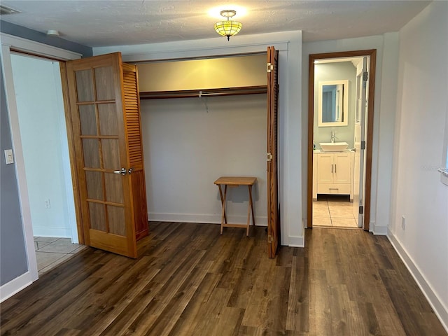 unfurnished bedroom with dark wood-type flooring, a closet, a sink, and baseboards