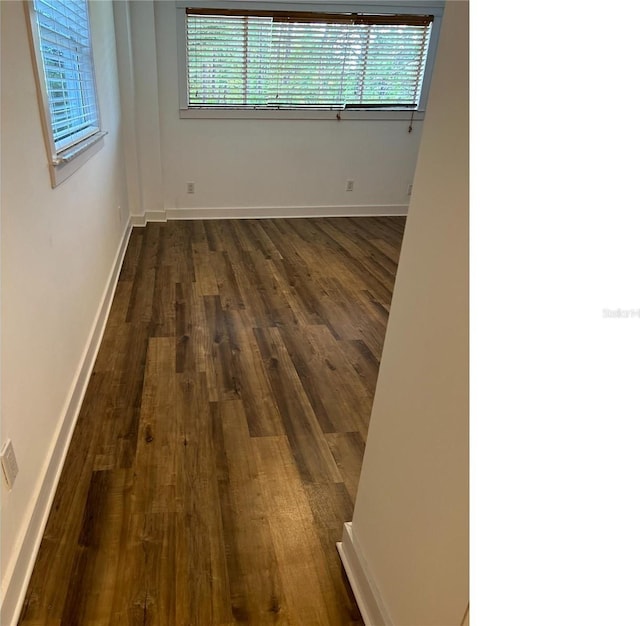 spare room featuring a healthy amount of sunlight, baseboards, and dark wood-style flooring