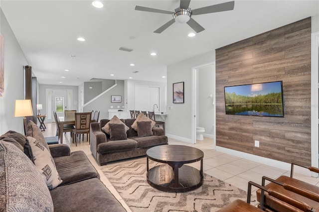 tiled living room with ceiling fan, wooden walls, and sink