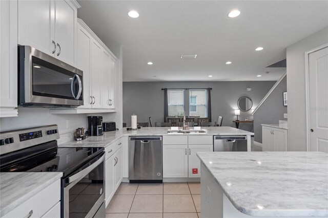 kitchen with sink, kitchen peninsula, light tile patterned flooring, white cabinetry, and stainless steel appliances