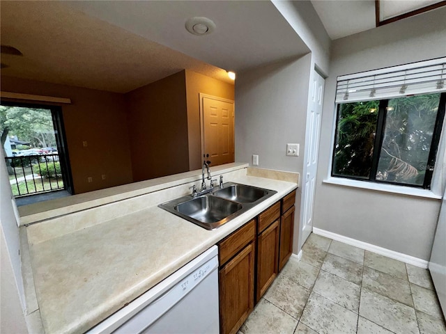 kitchen with white dishwasher, a sink, baseboards, light countertops, and brown cabinetry