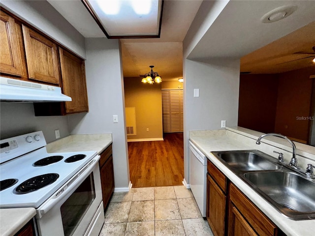 kitchen with under cabinet range hood, white appliances, a sink, baseboards, and light countertops