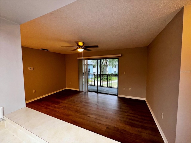 empty room with a textured ceiling, wood finished floors, visible vents, a ceiling fan, and baseboards