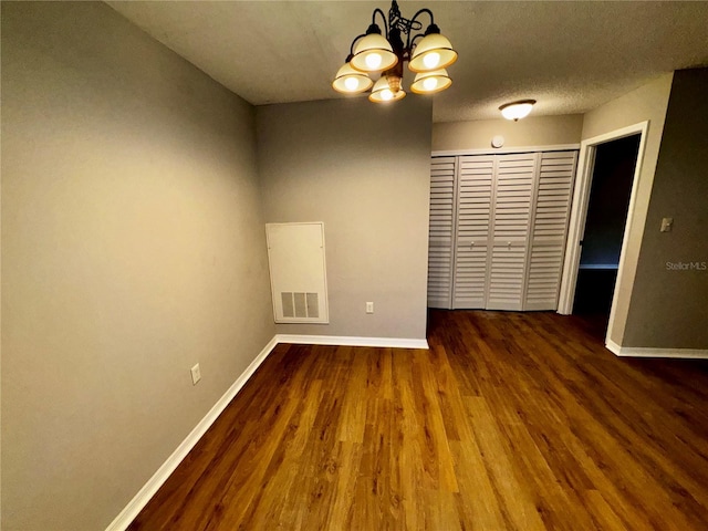 empty room featuring a textured ceiling, wood finished floors, visible vents, baseboards, and an inviting chandelier