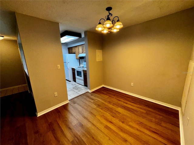 unfurnished dining area with a chandelier, a textured ceiling, baseboards, and wood finished floors