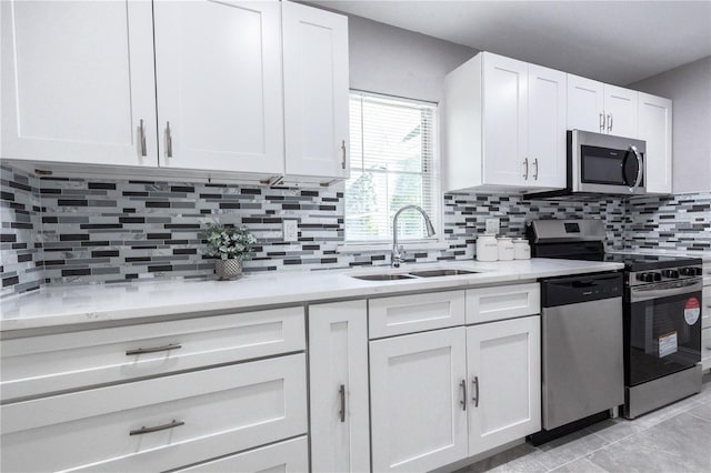 kitchen featuring light tile patterned floors, tasteful backsplash, appliances with stainless steel finishes, white cabinetry, and a sink