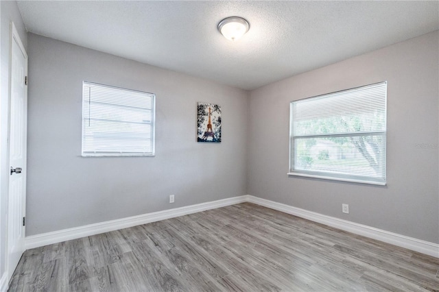 unfurnished room with light wood-type flooring and a textured ceiling