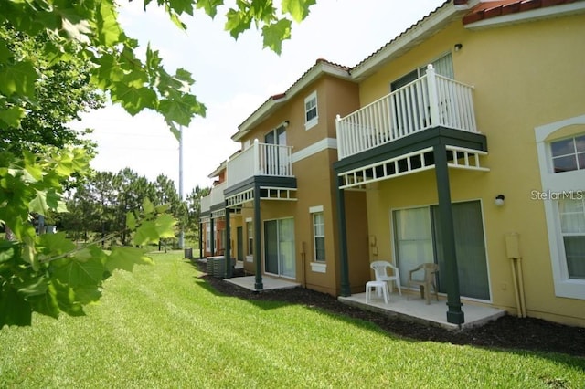 rear view of property featuring a balcony, a yard, and a patio