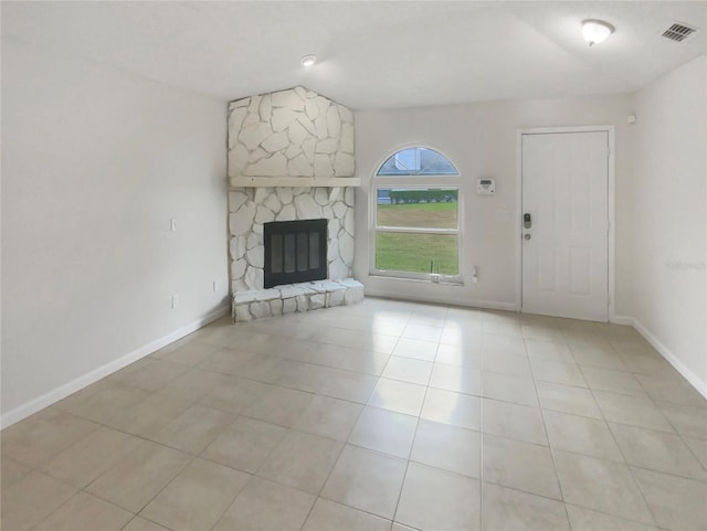 unfurnished living room featuring a stone fireplace, light tile patterned floors, and vaulted ceiling