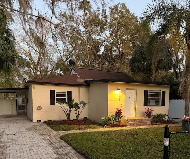 ranch-style house with concrete block siding, an attached carport, fence, decorative driveway, and a front lawn