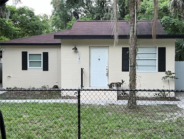 view of front of property with a shingled roof, fence, concrete block siding, and a front yard