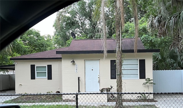 view of front of home featuring roof with shingles, concrete block siding, and fence