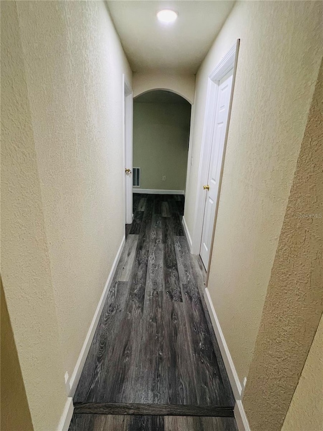 corridor featuring visible vents, arched walkways, dark wood-type flooring, and a textured wall