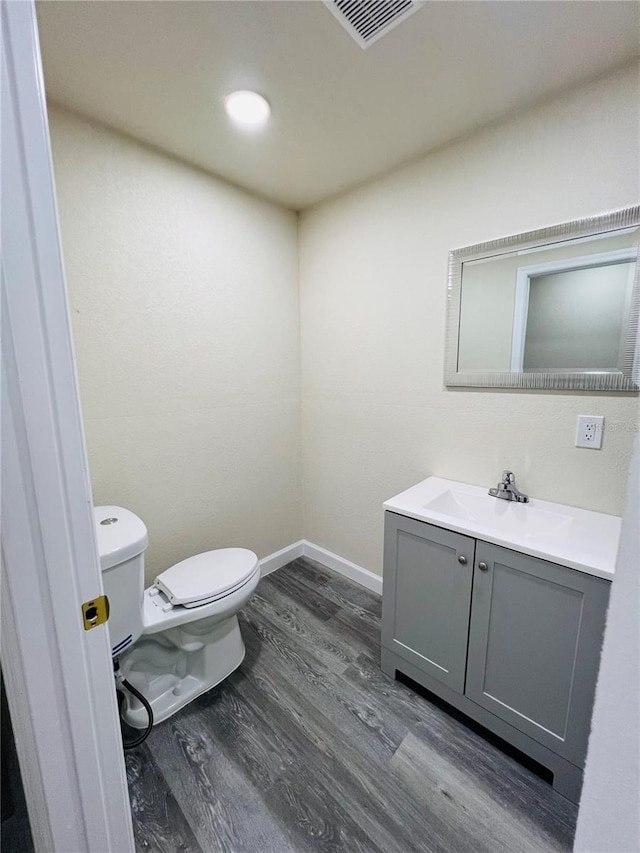 bathroom featuring baseboards, visible vents, toilet, wood finished floors, and vanity