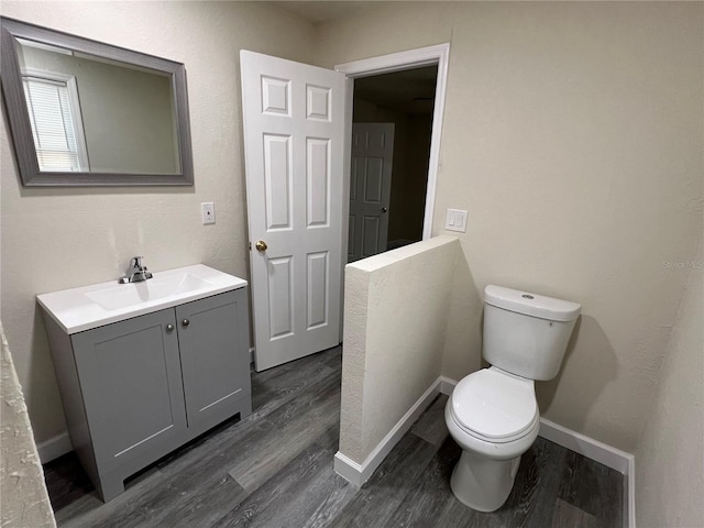 half bath featuring toilet, baseboards, wood finished floors, and vanity