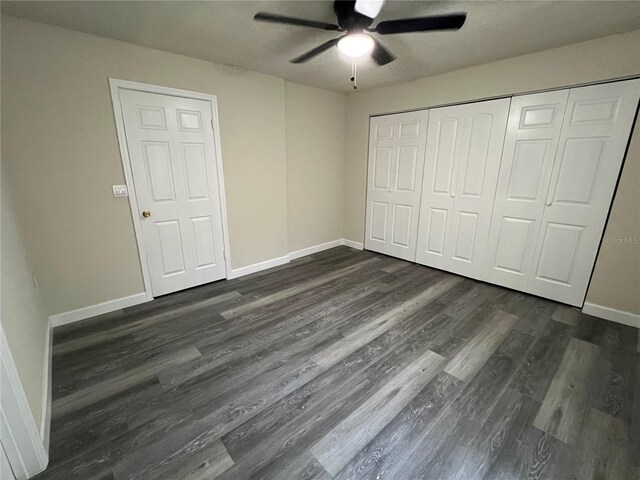 unfurnished bedroom with a closet, dark wood-style flooring, ceiling fan, and baseboards