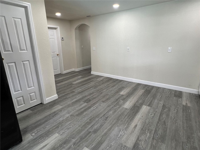 empty room featuring arched walkways, dark wood-style flooring, baseboards, and recessed lighting