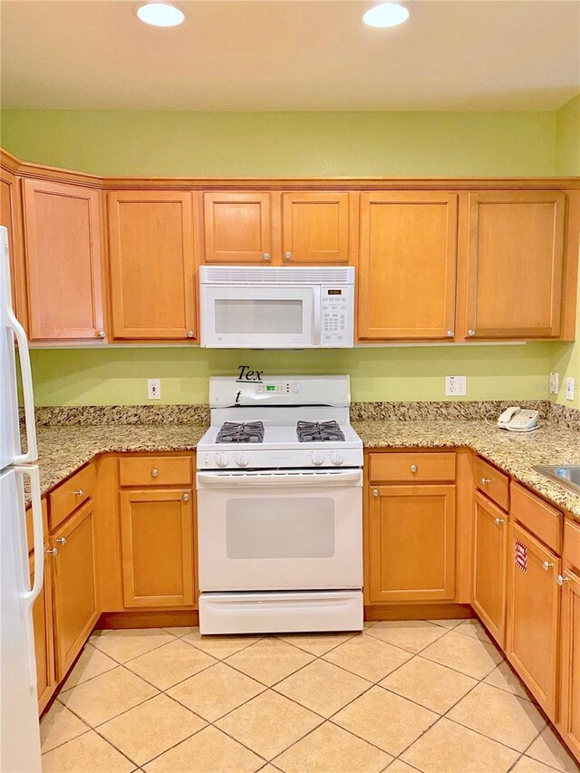 kitchen featuring light stone counters, sink, white appliances, and light tile floors